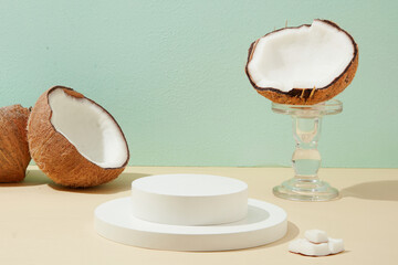 The white podium in the middle of the frame displays products with fresh coconuts decorated. Creative and sophisticated space. Cosmetics with fresh coconut extract.