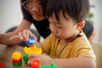 Asian cute brother and sister play with a toy block designer on the table in the living room at home. Concept of siblings bonding, friendship, and learning through play activity for kid development.