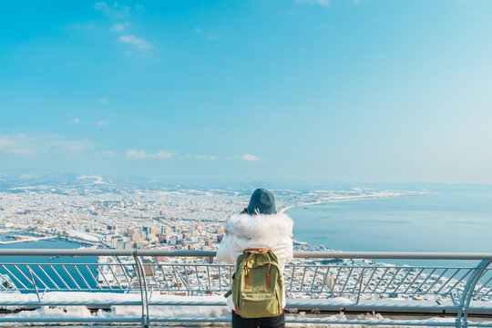 Woman tourist Visiting in Hakodate, Traveler in Sweater sightseeing view from Hakodate mountain with Snow in winter. landmark and popular for attractions in Hokkaido, Japan.Travel and Vacation concept