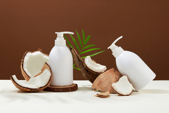 Unlabeled shower gel bottles containing coconut extract are displayed with coconut flakes of different sizes. Minimalist background with beauty theme.