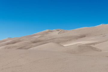 Arid sand dune landscape in direct sunlight with a bright blue sky at Great Sand Dune National Park in southern Colorado.