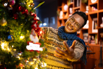 Cheerful Asian man is excited for Christmas night, decorating his Christmas tree in his living room.