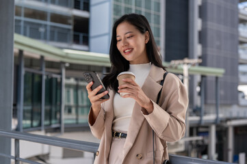A beautiful Asian businesswoman is responding to messages on her phone outdoors on a skywalk.