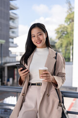 Fototapeta premium A beautiful Asian businesswoman is smiling at the camera and standing outdoors on a skywalk.