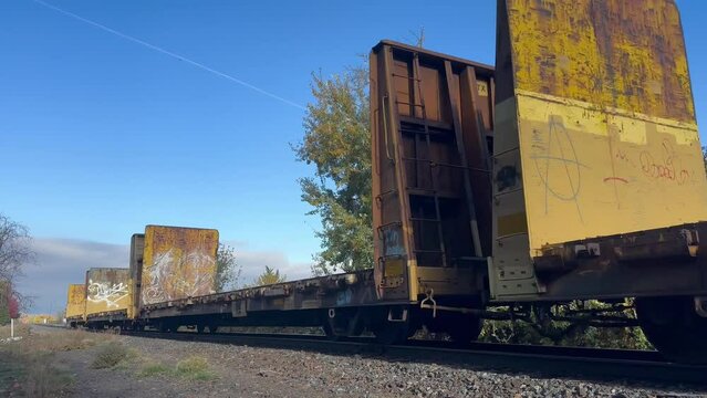 An empty freight train goes over railroad tracks on a blue-sky day.