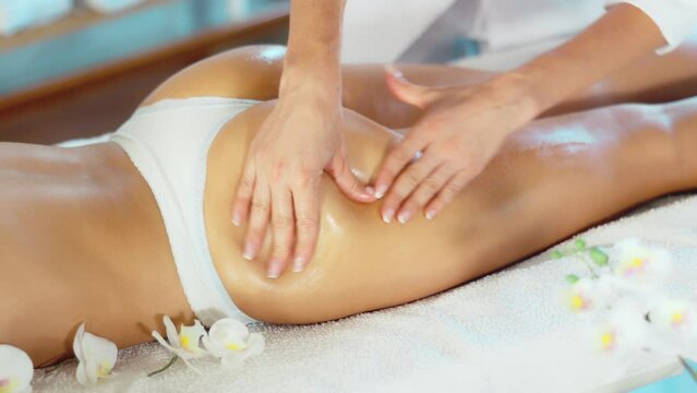 Female masseuse doing massage of thighs and buttocks close-up to young woman client