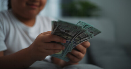 Portrait close up hands of young Asian woman enjoy counting cash dollars banknotes on sofa in the living room at home.