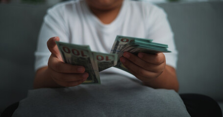 Portrait close up hands of young Asian woman enjoy counting cash dollars banknotes on sofa in the living room at home.