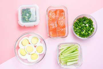 Cut food in glass lunch boxes on pink background close-up, top view.