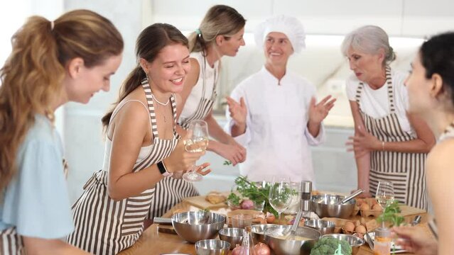 Young woman drinks wine and talks to group during cooking master class