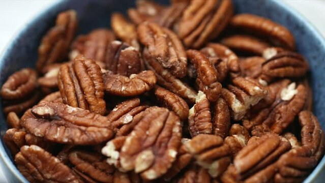 Pecan nuts rotating in blue bowl. whole food raw pecans. HD shallow depth of field image of wholegrain foods for plant-based and vegan diet and recipes.
