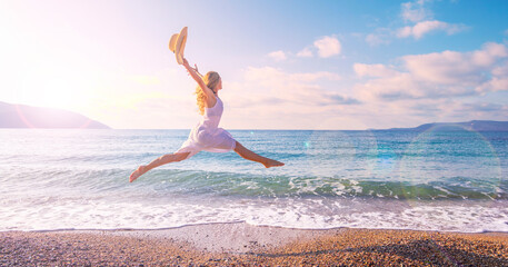 Happy tourist woman in a white dress enjoys beautiful beach at sunset - obrazy, fototapety, plakaty