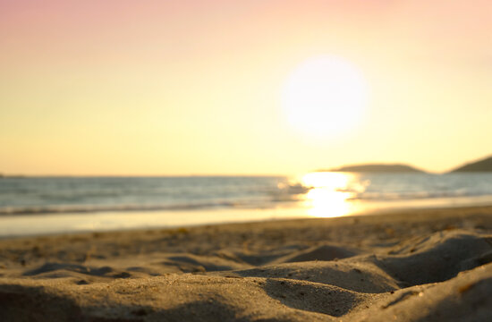 Beach sand background for summer vacation concept. The nature of the beach and the summer sea with the soft sunlight hitting the sand. The sea sparkles against the sunset sky.