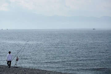 Fototapeta na wymiar 朝の海岸で海釣している若い女性の姿