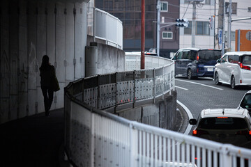 街のトンネルを通過する車の列と歩く一人の女性の後姿