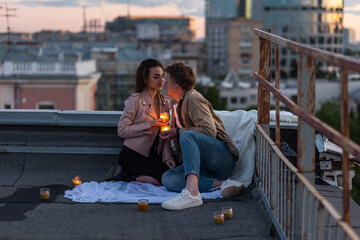 Surprise date on rooftop with urban cityscape and skyscrapers on background. Happy young loving couple drinking wine having romantic candlelit dinner celebrating anniversary or Valentines Day