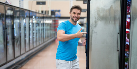 Young man as a customer in front of the refrigerated shelf in the supermarket. Store, shopping,...