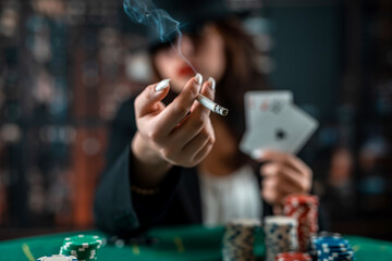 Female hand with playing cards and poker chips and burning cigar close-up in front of poker table....