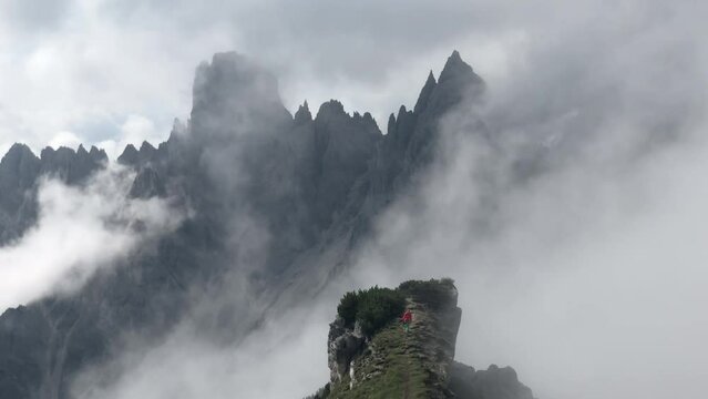 Man with red jacket standing on one degree, behind him mountain peaks and pointed rocks, dramatic clouds, Cimon the Croda Liscia and Cadini group, Auronzo di Cadore, Belluno, Italy, Europe