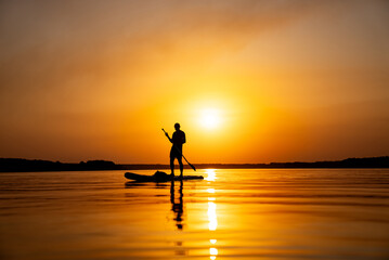 A person standing on a paddle board in the water. A Serene Moment: Stand-Up Paddleboarding on the...