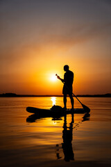 A Serene Moment: Man Standing on Paddle Board in Crystal Clear WatersA man standing on a paddle board in the water.