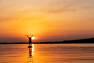 A Serene Sunset Surfing Experience. A person standing on a surfboard in the water at sunset