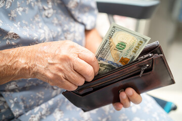 Asian senior woman holding and counting US dollar banknotes money in purse. Poverty, saving problem...