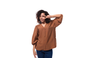 young cute caucasian woman with curly black hair dressed in a brown shirt on a white background...
