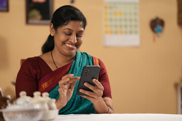 happy smiling Indian middle aged woman using mobile phone at home - concept of technology, social media sharing and communication