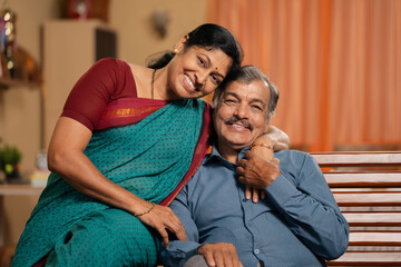 happy smiling 50s senior couple looking at camera while spending time together at home - concept of family togetherness, relationship bonding and companionship