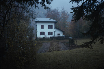 An isolated house in the forest near Lake Cei, at blue hour, in the Northern Italy, during a rainy autumnal day