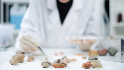 A female geologist or archaeologist is analyzing a sample of rock or mineral in paleontology,...