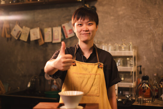 A confidence, prouded and smart female or LQBTQ coffee shop entrepreneur or barista is wearing apron stand with inspiration. Work life balance. Startup SME business. Happiness while working with job.