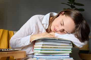 Young woman student with many books feeling fatigue after long hours studying sleeping on stack of books in home interior, falling asleep while preparing for test.