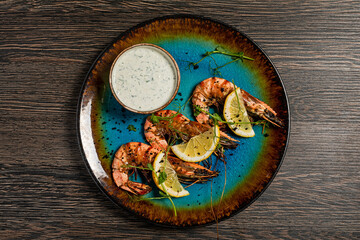 Grilled tiger shrimp with lemon, tzatziki sauce, microgreens served on blue plate, top view - 673651965