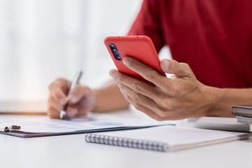 Fototapeta premium Close up hand of man writing notes while making phone call and using laptop at home