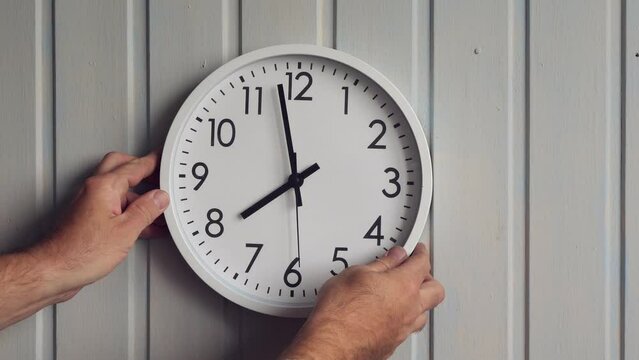 a man hangs a round clock on a wall in the room. the clock shows 8 o'clock or 20 o'clock.