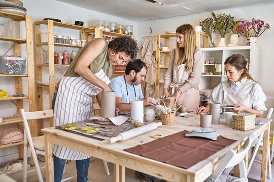 Group of people in aprons making ceramic crafts together in a workshop. Hobby and craft concept.