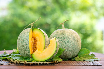 Orange Melon on blurred greenery background, Orange Melon or Cantaloupe fruit in Bamboo mat on wooden table in garden. - obrazy, fototapety, plakaty