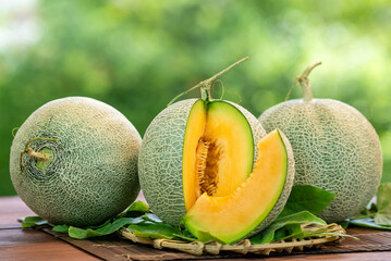 Orange Melon on blurred greenery background, Orange Melon or Cantaloupe fruit in Bamboo mat on wooden table in garden. - obrazy, fototapety, plakaty
