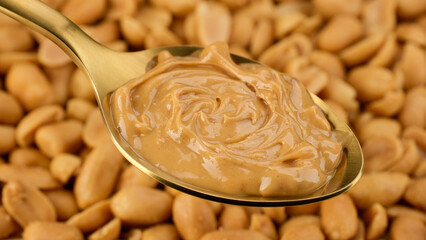 Peanut butter in golden spoon and peanuts on background