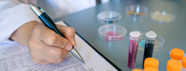 Banner of unrecognizable female scientist hand filling investigation form about dangers of small plastic particles on glitter. Close up of woman chemist analyzing microplastics on cosmetics.