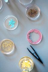 Top view of different glitter samples in petri dishes over a lab table background. Study of microplastics composition concept. Dangerous small plastic particles behavior to humans and environment.