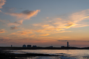 Naklejka premium Kjolnes lighthouse on the rocky shores of Barents Sea in soft and colorful evening light after sunset