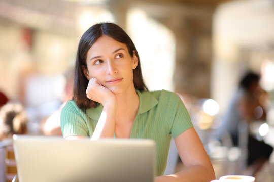 Woman with laptop thinking looking at side in a bar