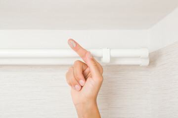 Young adult woman hand finger showing dust from top of white curtain rods in room. Closeup....