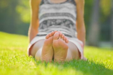 Young adult woman sitting and resting on fresh green grass in sunny warm summer day. Barefoot...