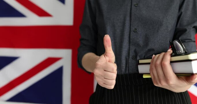 Woman promoting language learning with textbooks. English lecturer stands in front of British flag showing thumb up as approval in school slow motion