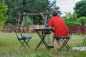Samotny mężczyzna siedzi sam przy stole w ogrodzie i myśli  - obrazy, fototapety, plakaty