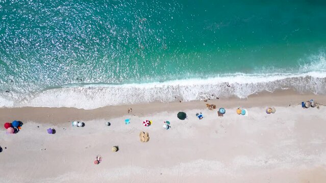 Overhead drone of beach umbrellas on a sandy shore and close to the waves